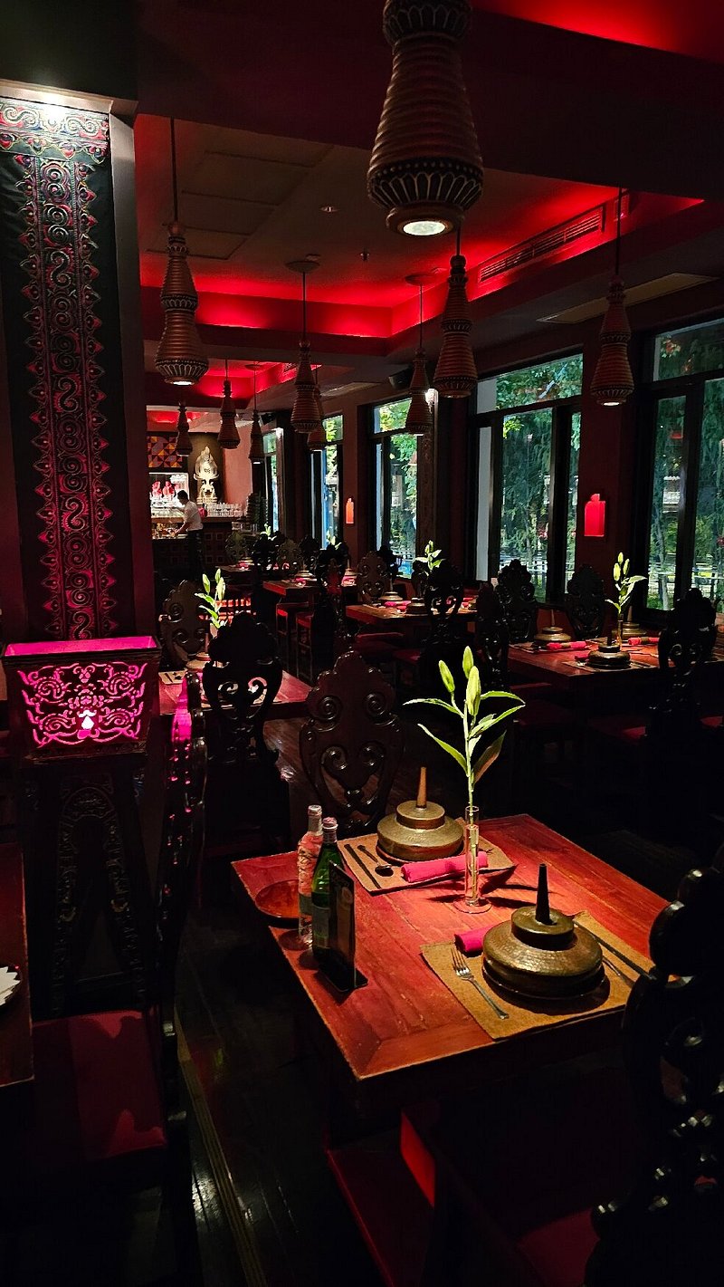 The moody, candlelit dining room — crimson silk, rattan lanterns, dark wood carvings from remote Yunnan villages