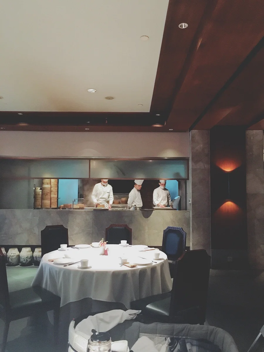 The elegant dining room at Xin Rong Ji Jing'an — muted greys, warm brass, and floor-to-ceiling windows overlooking a private courtyard